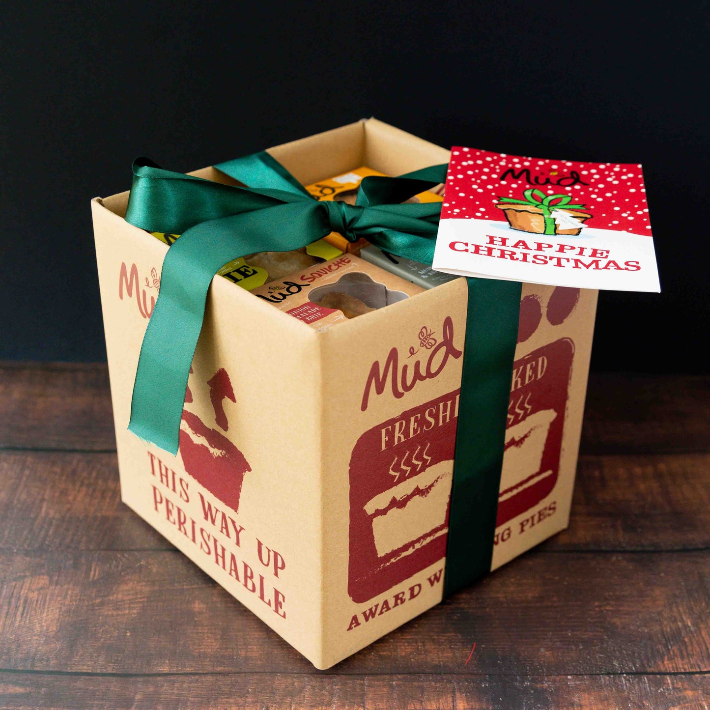 Cardboard box with red pie graphics, festive ribbon, and "Happy Christmas" card—Mud Pies Best Ever Vegetarian Christmas Gift Box.