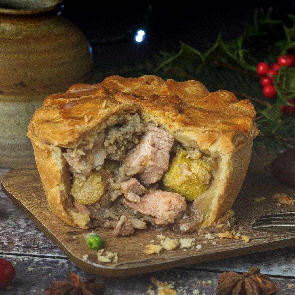 Mud Pies’ golden, flaky steak and ale pie, sliced to show meat, peas and chestnuts, rests on a board amid festive greenery and berries.
