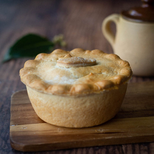 Mud Pies Steak and Kidney Pie, golden-brown with crimped edges and a flaky pastry lid, sits on a board radiating homely warmth.