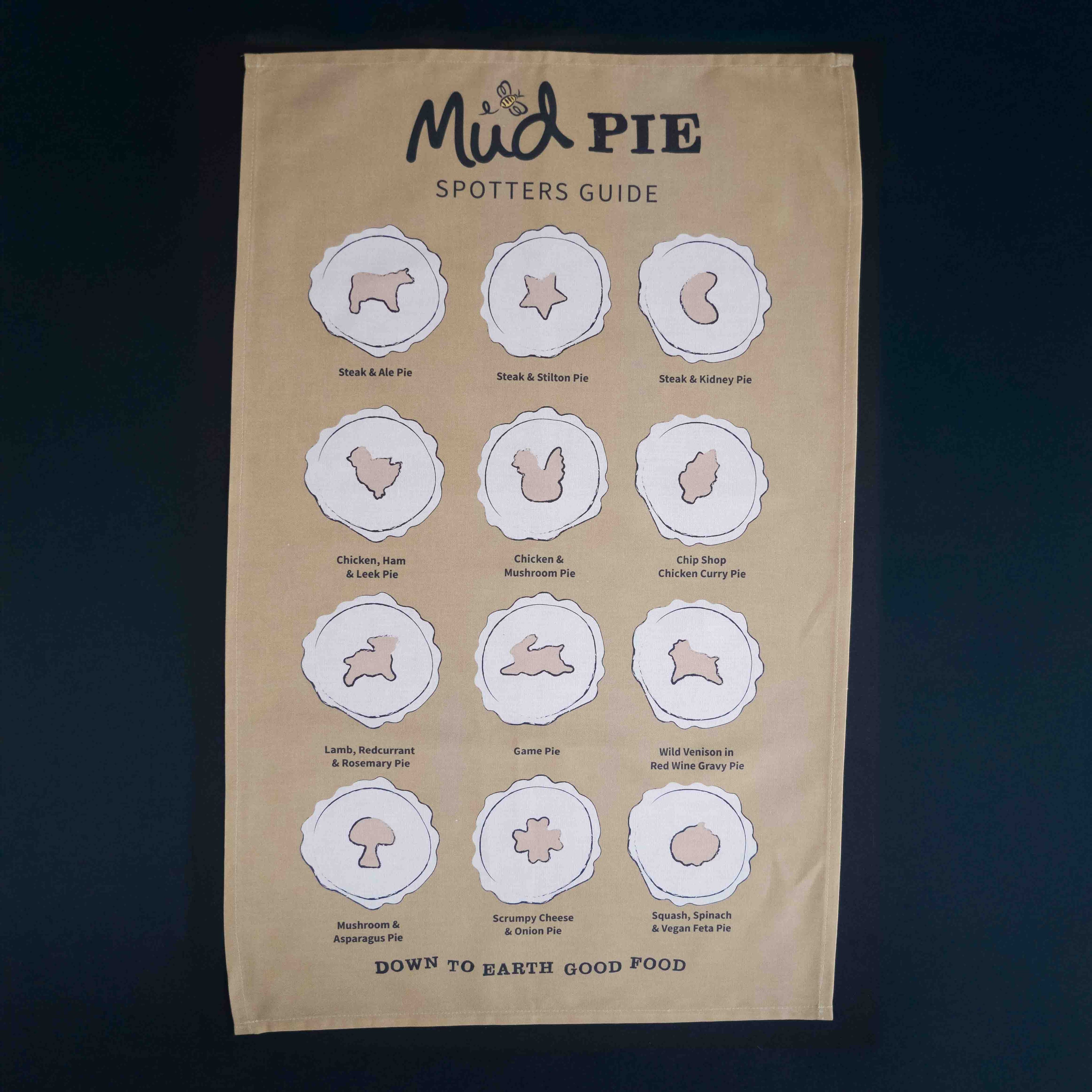 The Mud Pies Tea Towel Pie Spotters Guide is a beige, pure cotton towel with twelve outlined pies and “Down to Earth Good Food.”.