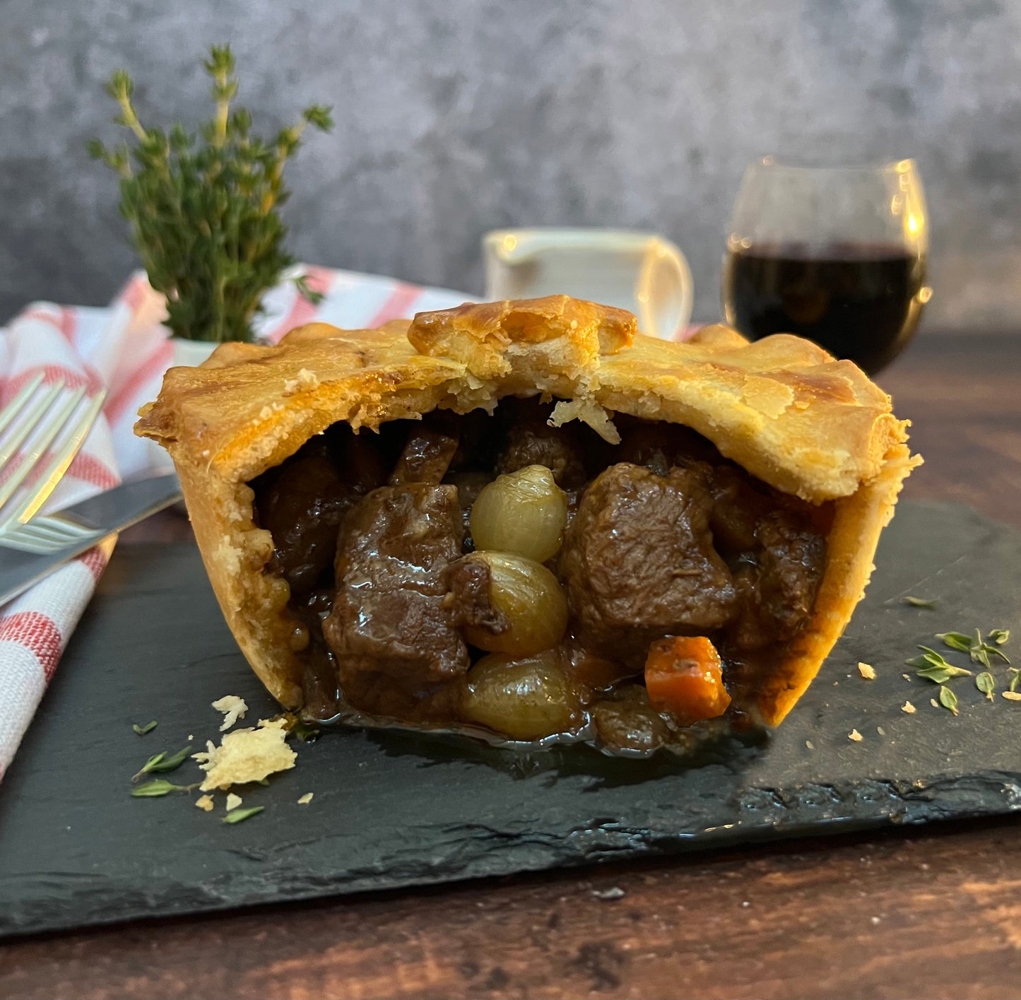 Half-eaten meat pie on a slate board with a glass of red wine in the background.