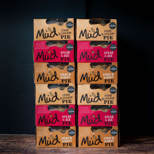 Mud Pies Steak Pie Box packs, in brown Stilton and red Ale varieties, are stacked in rows with windows and Great Taste awards.