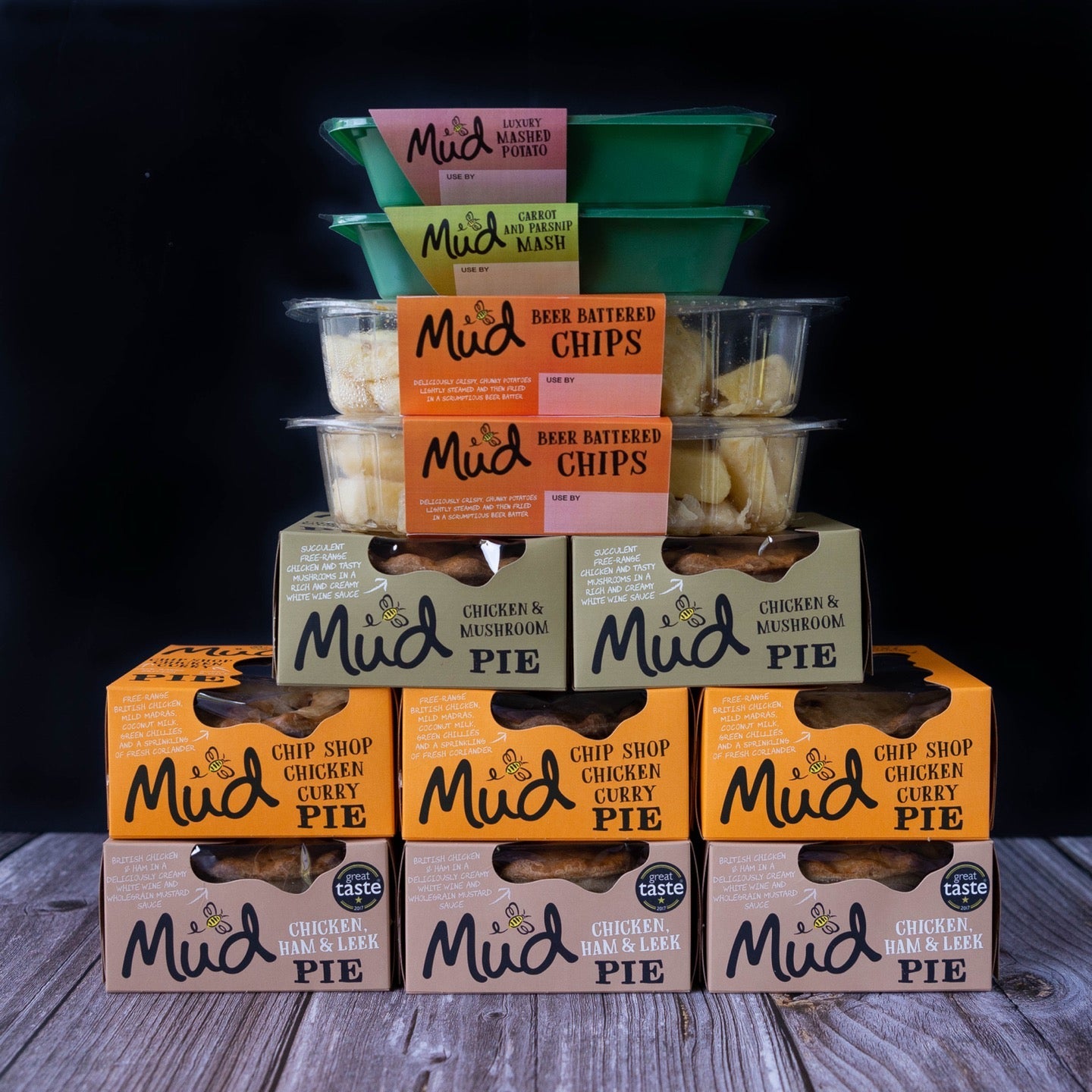 Mud Pies' Chicken Dinner selection: chunky chicken pies, beer battered chips in clear tubs, and mashed potato cups on wood.