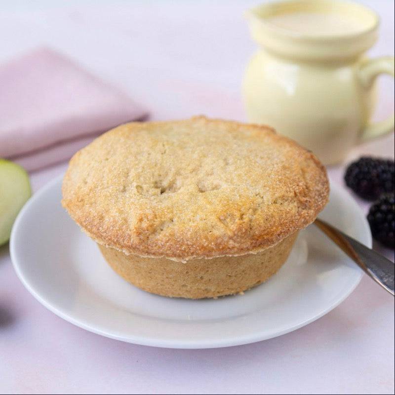 Mud Pies’ Apple and Blackberry Pie, golden-brown pastry on a white plate, with green apple, blackberries, yellow jug of cream and fork.