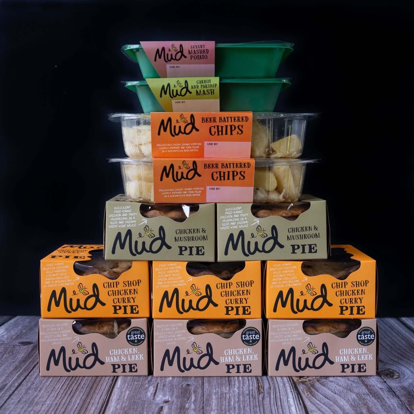 Mud Pies' Chicken Dinner selection: chunky chicken pies, beer battered chips in clear tubs, and mashed potato cups on wood.
