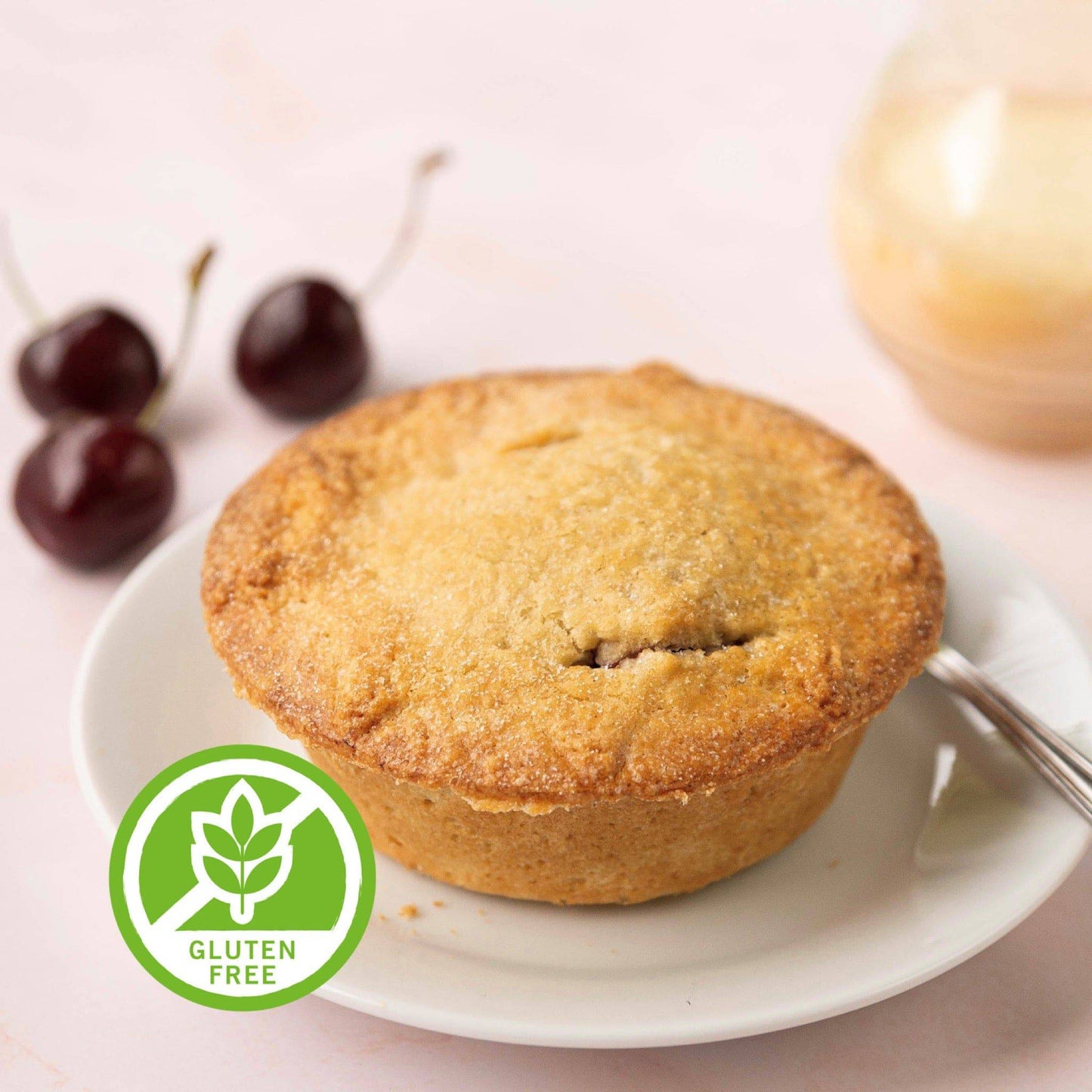 Mud Pies Gluten-Free Black Cherry Pie sits golden-brown on a white plate with a spoon, cherries and jar behind, green Gluten Free badge.