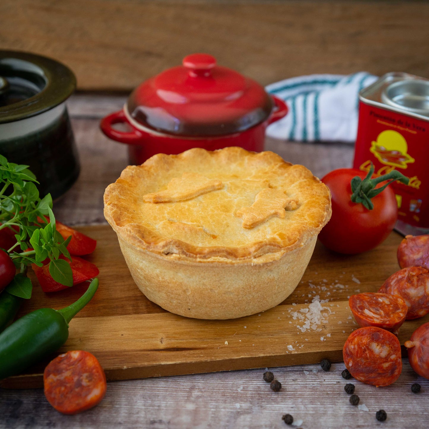 Mud Pies’ Chicken and Spanish Chorizo Pie rests golden-brown on a wooden board, topped with basil, jalapeños, chorizo and tomato.