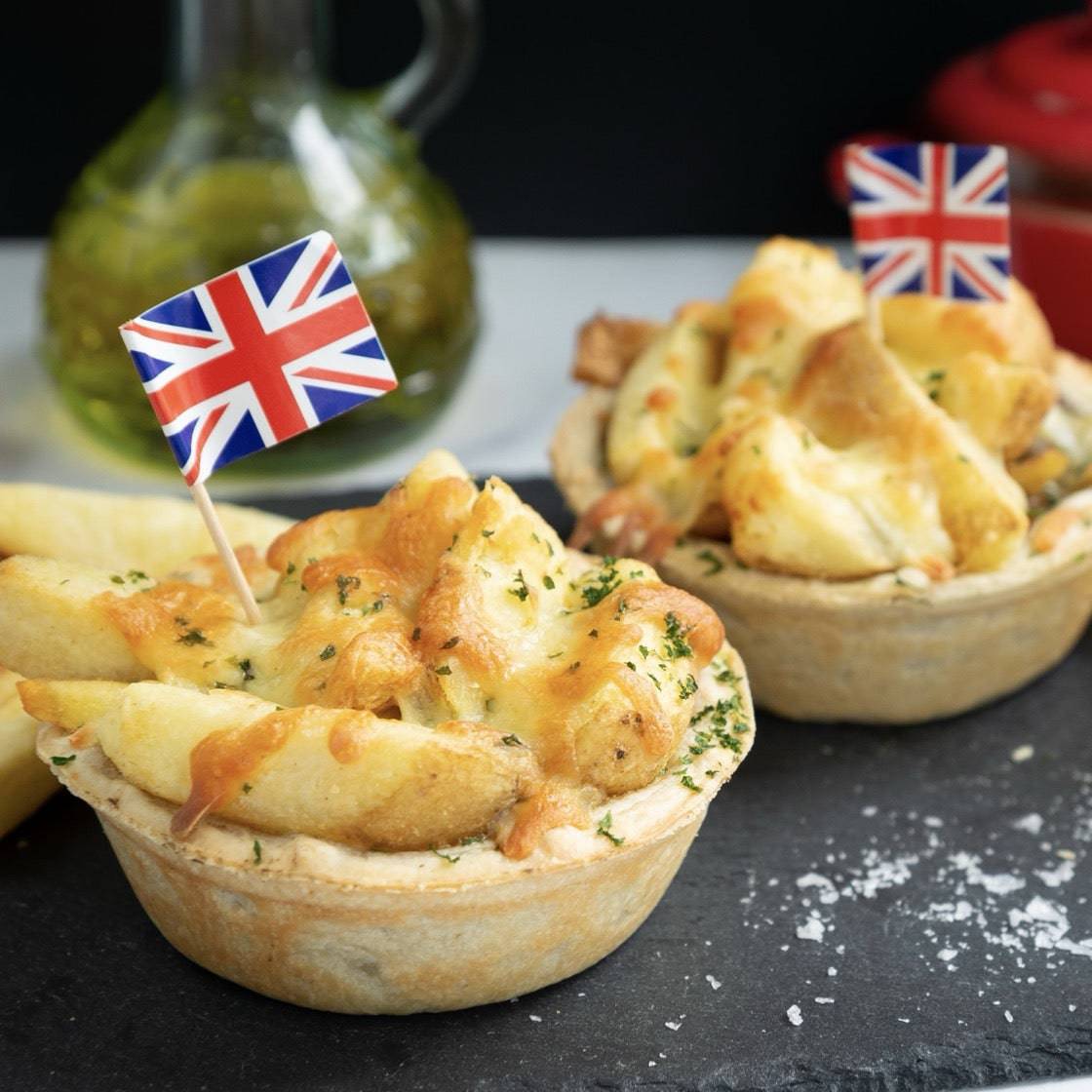 Chip Top Chicken Royale pies by Mud Pies, packed with chips and gooey cheese, crowned by tiny UK flags on salty dark slate.