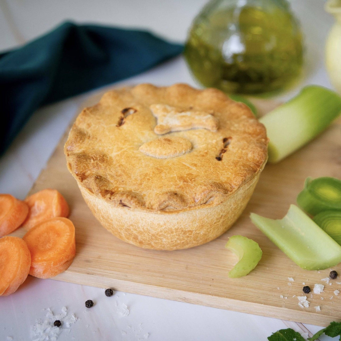 Mud Pies’ Spring Lamb and Mint Pie, topped with a lamb pastry cut out, rests on a wooden board with carrots, leeks, celery, salt and peppercorns.