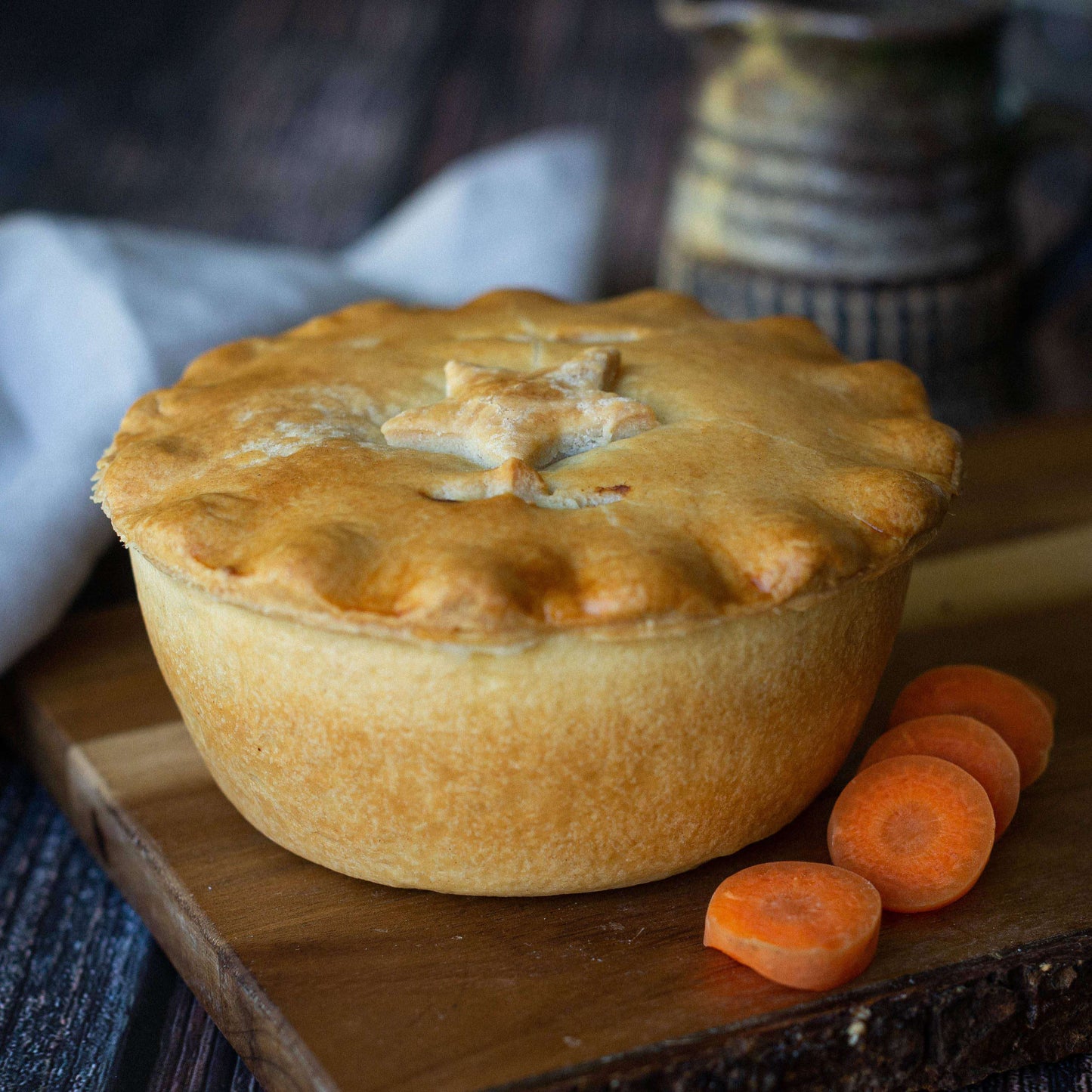 Mud Pies’ Steak and Stilton Pie, finished with a golden star-shaped pastry lid, sits on a wooden board next to three carrot slices.