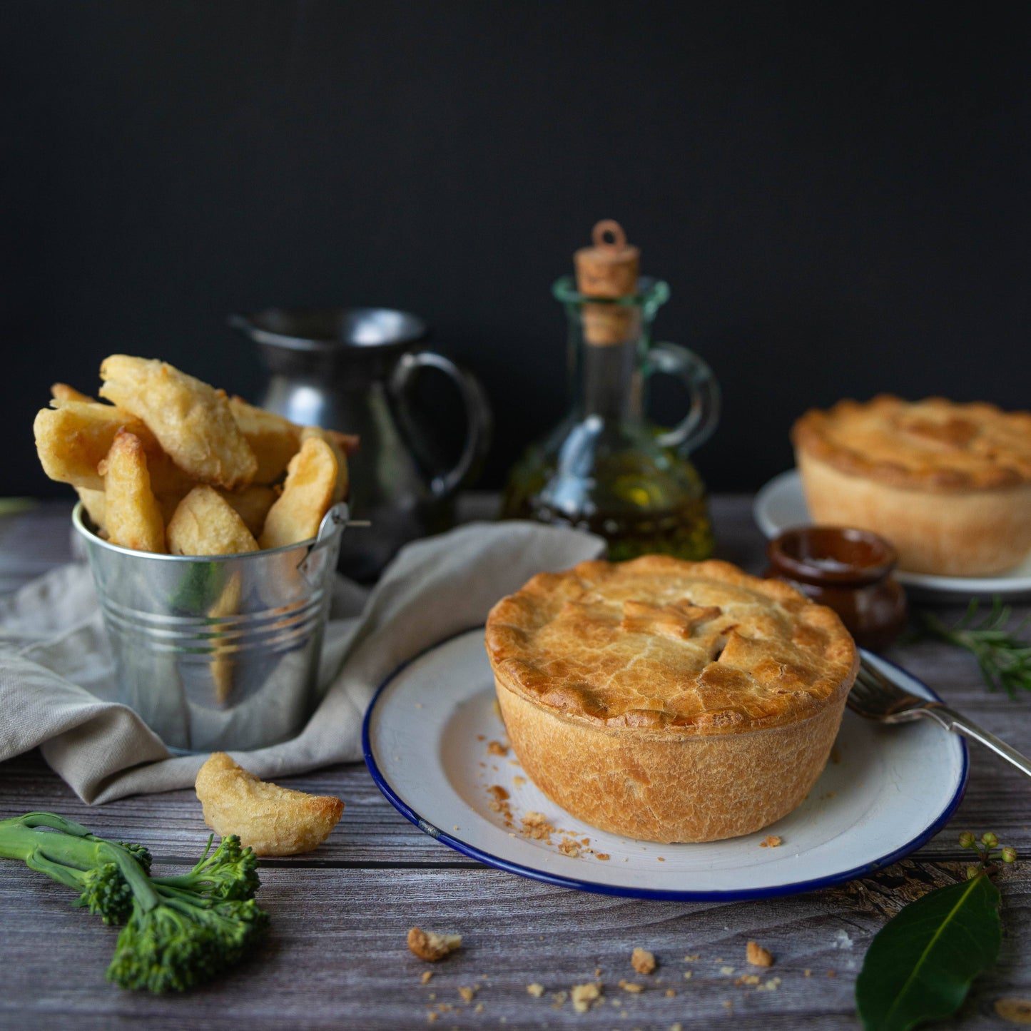 Mud Pies pie, golden and crisp on a blue-rimmed plate, with beer battered chips, sauces, and oils atop a rustic pub table.