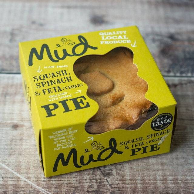 Mud Pies Squash, Spinach and Feta Pie vegan in a yellow box on wood, revealing golden pastry and boasting local, plant-based ingredients.
