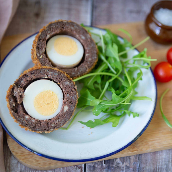 Scotch egg cut in half on a plate with some rocket