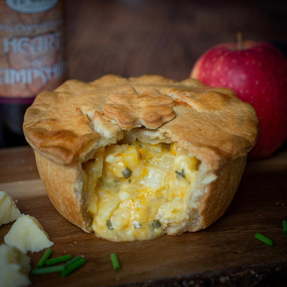 The Mud Pies Best Ever Vegetarian Christmas Gift Box: golden veggie pie, cheese cubes, chives, and red apple on wood.