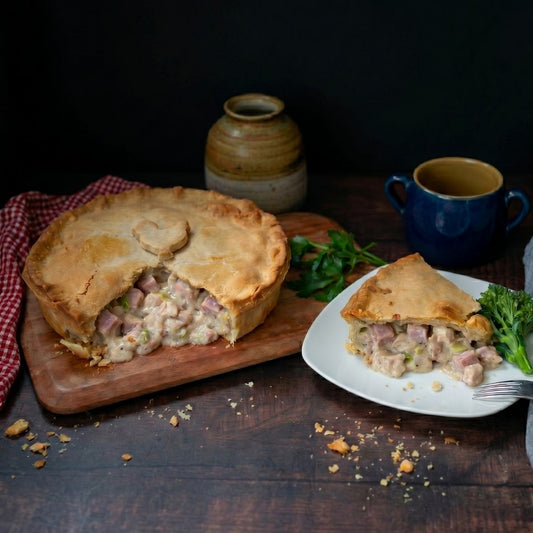 Chicken, Ham Leek Family Pie by Mud Pies on wooden board with broccolini, rustic tableware and parsley; serves four.