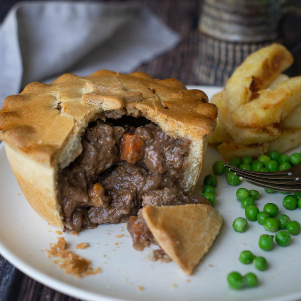Mud Pies’ Steak and Stilton Pie boasts golden shortcrust pastry packed with beef, carrots, rich gravy; wedges and peas beside.