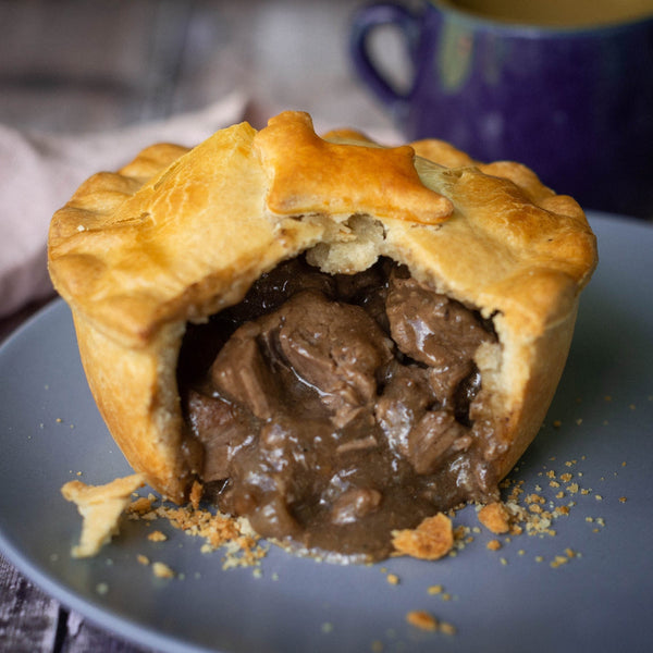 Mud Pies' Wild Venison In Red Wine Gravy rests on a grey plate, golden pastry sliced open to show juicy meat and rich sauce inside.