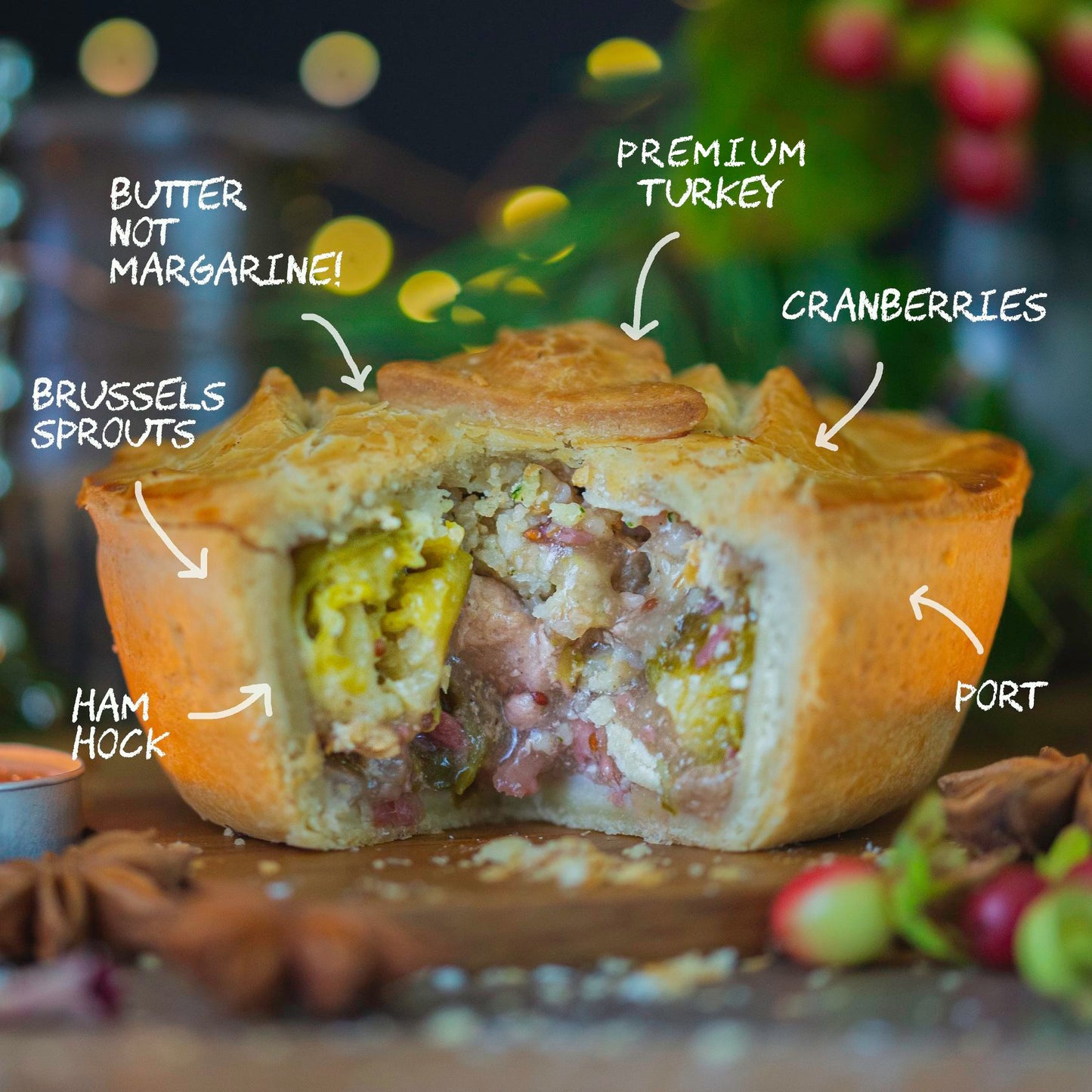 A golden Mud Pies Christmas In A Pie, sliced to reveal turkey, ham hock, sprouts, cranberries in pastry; labels and blurred festive decor.