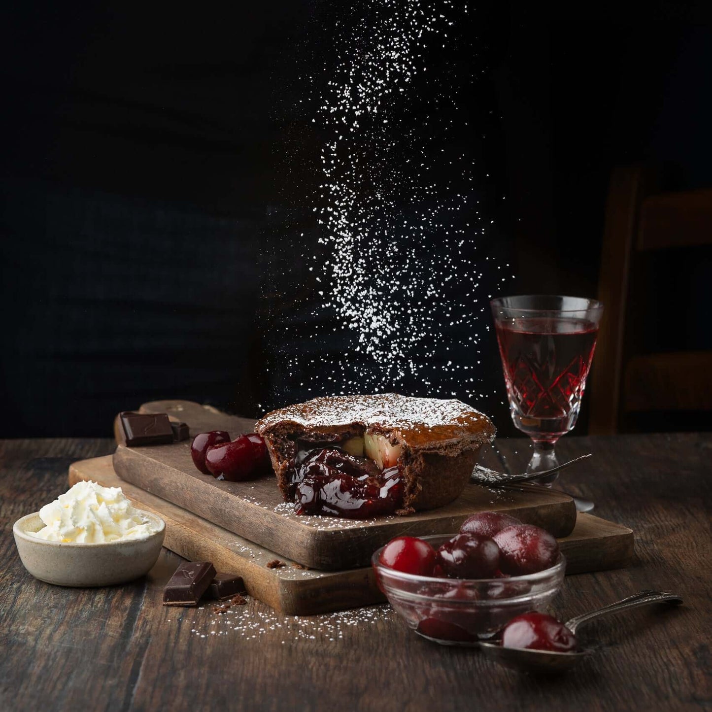 Mud Pies’ limited edition Black Forest Gateau Pie, filled with rich cherry compote and icing sugar, on a board with cherries, chocolate, cherry cordial and whipped cream.