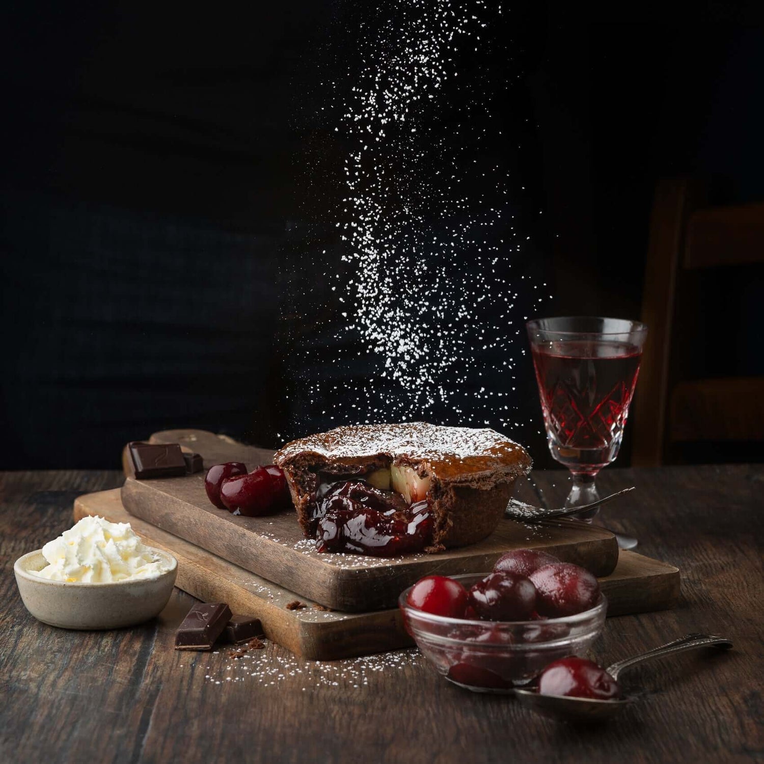 Mud Pies’ limited edition Black Forest Gateau Pie, filled with rich cherry compote and icing sugar, on a board with cherries, chocolate, cherry cordial and whipped cream.
