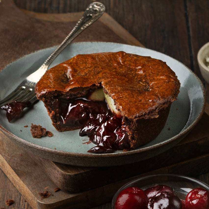 Mud Pies’ limited edition Black Forest Gateau Pie, golden crust and rich cherry filling, on a grey plate with fork and cherries.