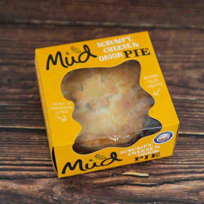 Mud Pies Scrumpy Cheese and Onion Pie (Cheese, Onion and Potato Pie) in a yellow box with a clear window, highlighting buttery pastry and Hampshire cider, on wood table.