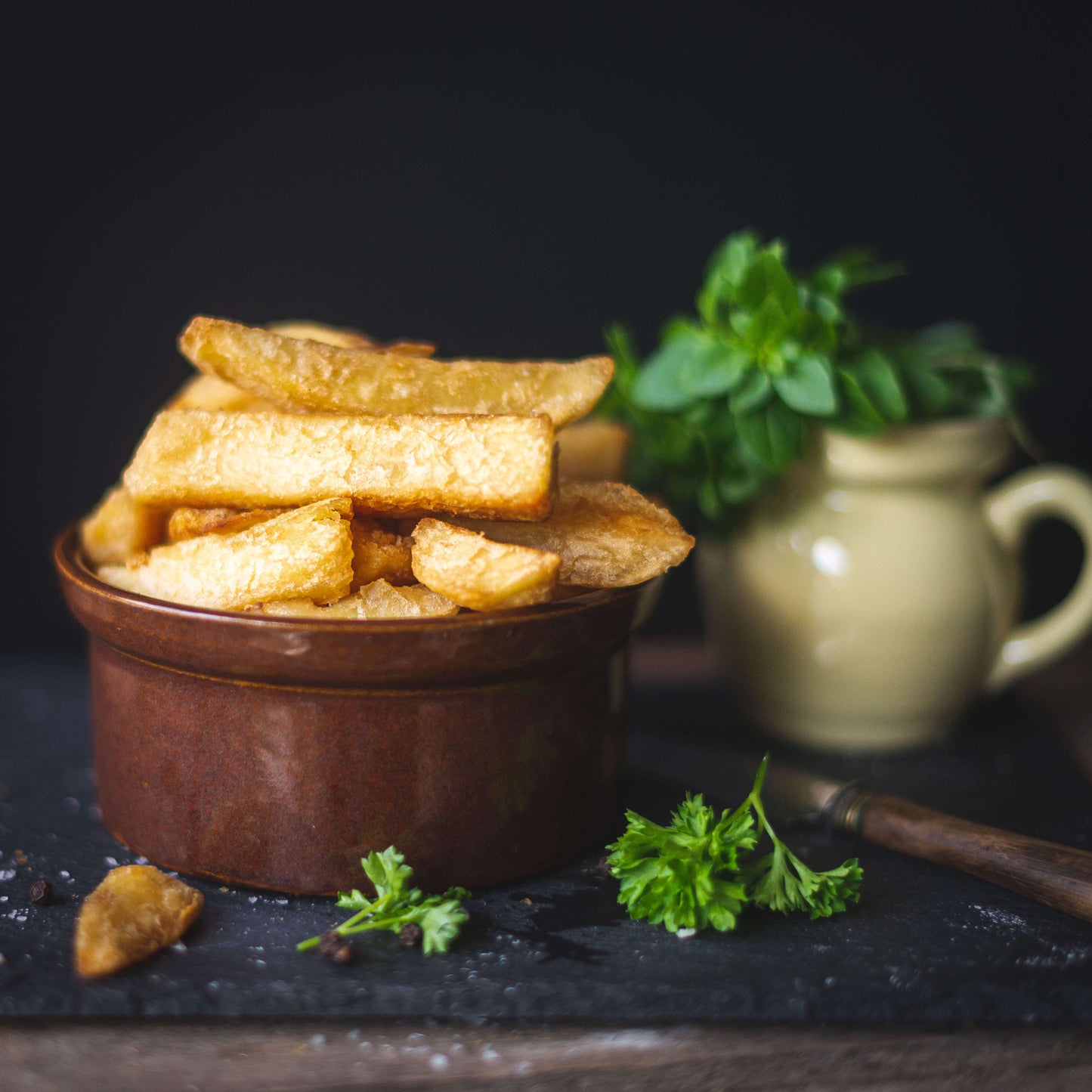 Mud Pies' The Complete Gift Box features a brown ceramic bowl of golden, crispy fries on a dark surface, with parsley, a beige jug of herbs, and savoury pies adding rustic charm.