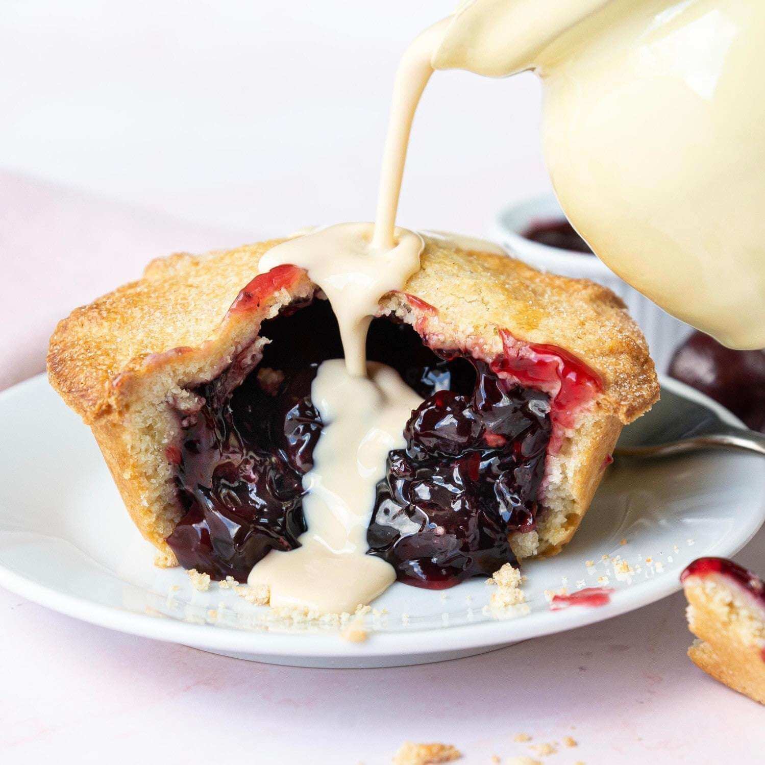 Mud Pies' Best Ever Vegetarian Christmas Gift Box golden mini pie on a white plate, split to reveal glossy cherry filling and thick cream.