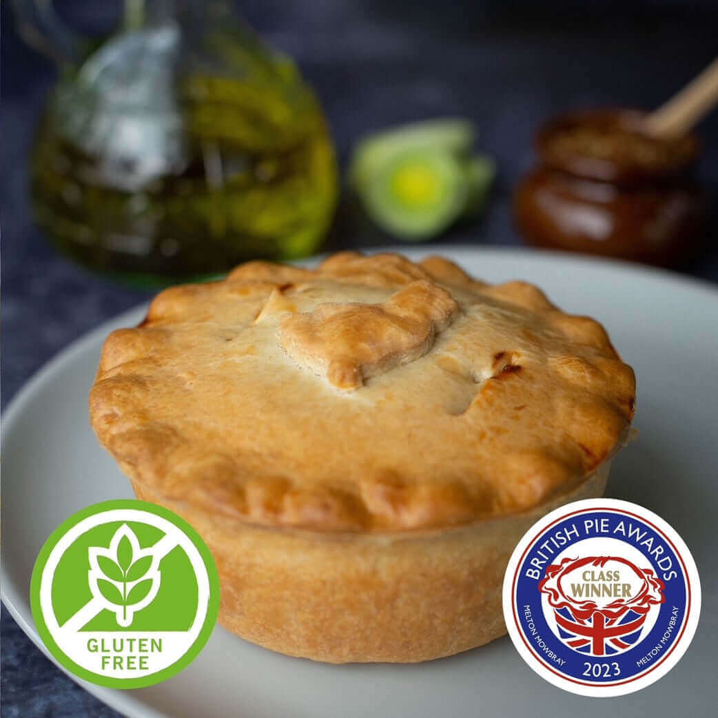 Mud Pies Gluten-Free Chicken, Ham and Leek Pie, golden-brown on a white plate, with award badges; oil bottle and honey dipper behind.