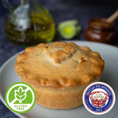 Mud Pies Gluten-Free Chicken, Ham and Leek Pie, golden-brown on a white plate, with award badges; oil bottle and honey dipper behind.