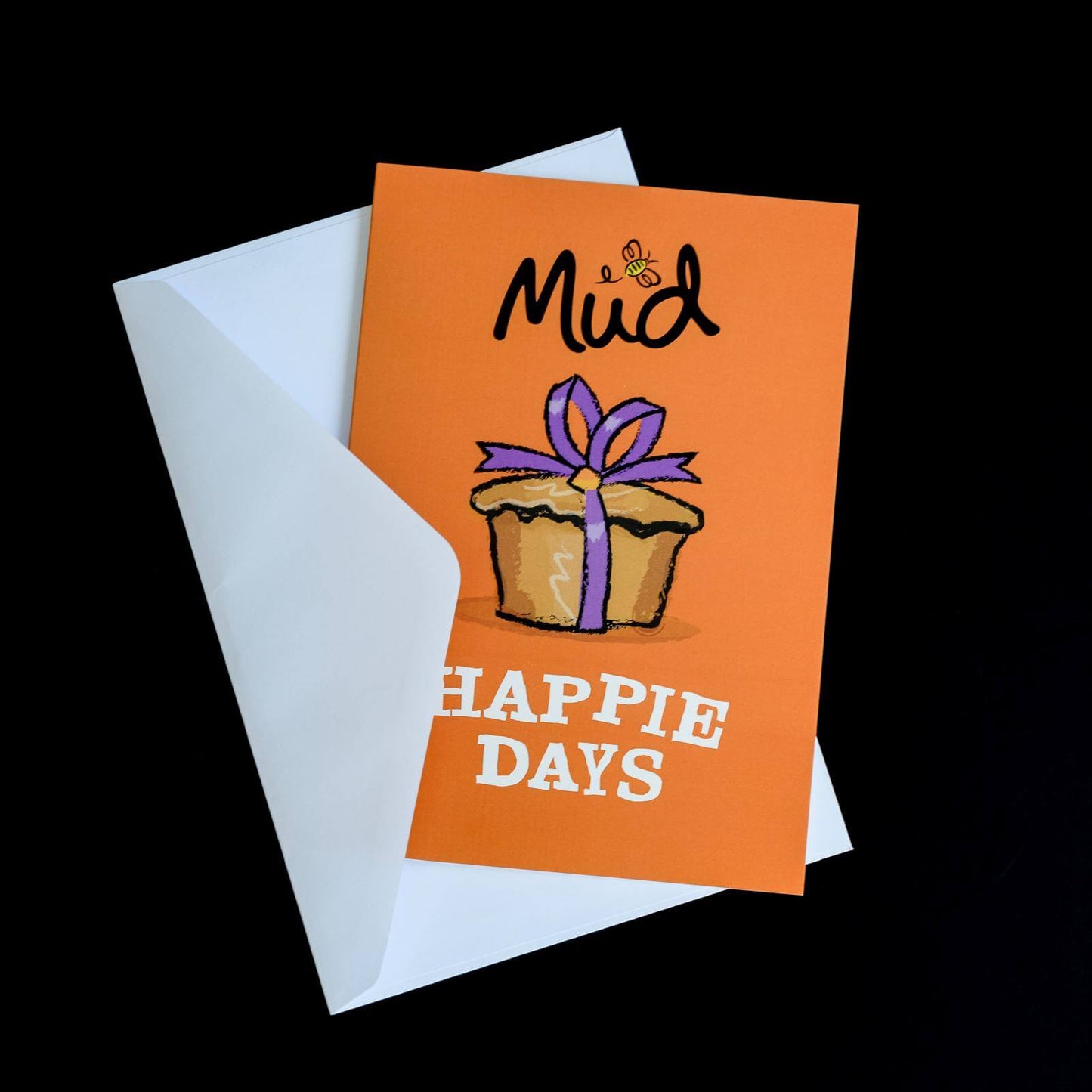The Happie Days Greetings Card by Mud Pies, an orange personalised card, shows a cake with purple ribbon and "HAPPIE DAYS" in white.