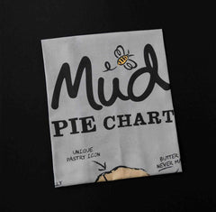 Tea Towel Pie Chart by Mud Pies—folded grey 100 cotton, on black surface, with “Mud PIE CHART”, bee and pie graphics.
