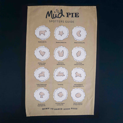 The Mud Pies Tea Towel Pie Spotters Guide is a beige, pure cotton towel with twelve outlined pies and “Down to Earth Good Food.”.