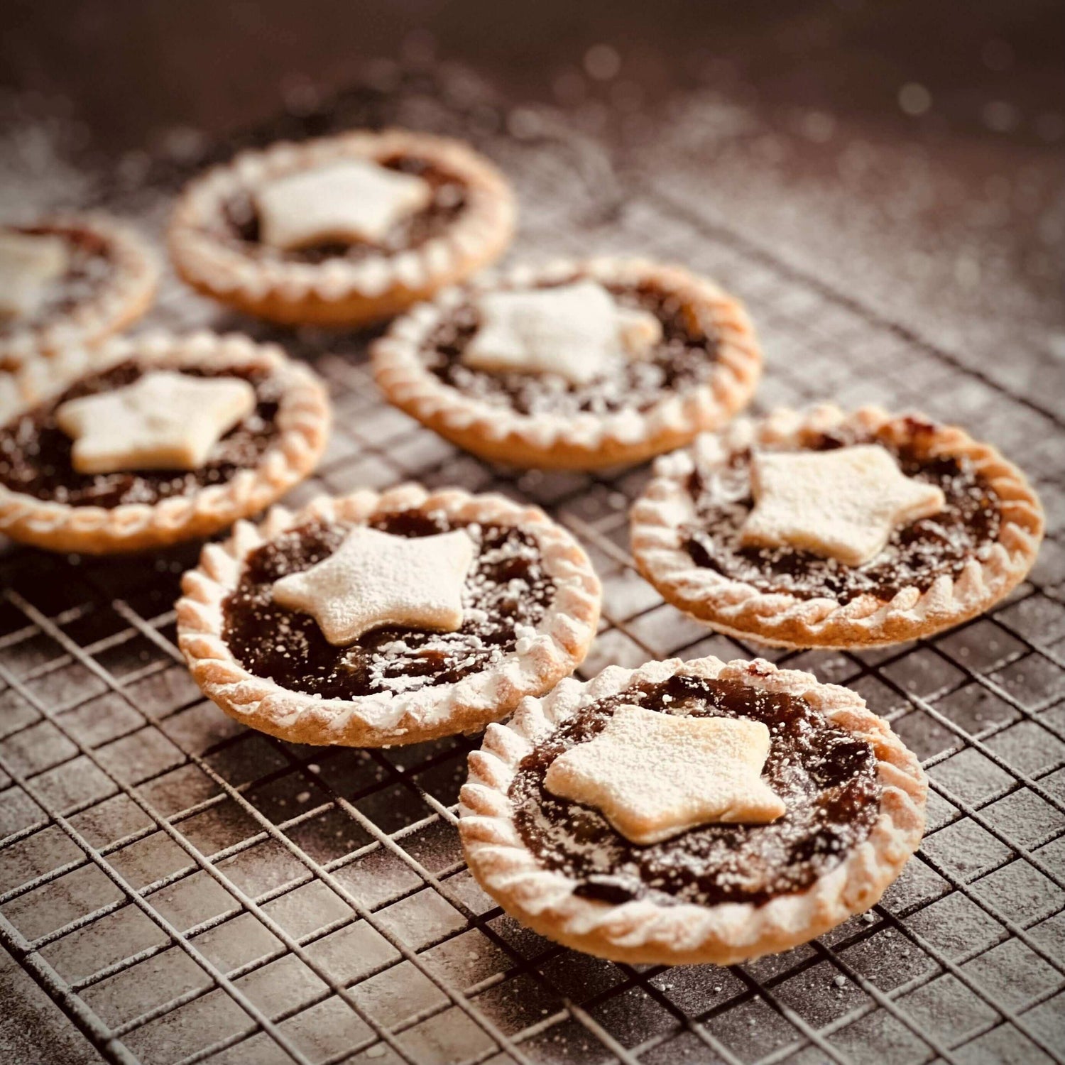 Mud Pies Brandy Laced Luxury Mince Pies—six close up, each crowned with a star pastry and dusted with icing sugar on a rack.