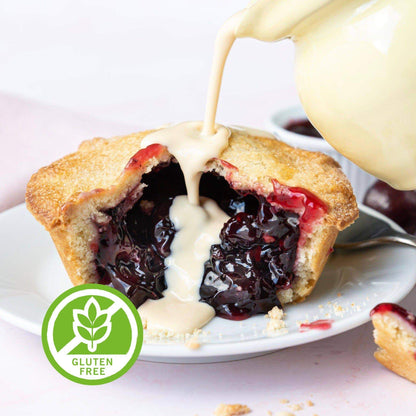 Mud Pies Gluten-Free Black Cherry Pie split open on a white plate, glossy filling exposed as cream pours over, with crumbs, spoon and green Gluten Free badge.