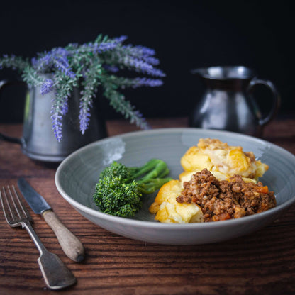 Mud Pies’ Shepherd’s Pie with local lamb atop mash and broccoli sits on a wooden table; metal jugs and lavender behind.