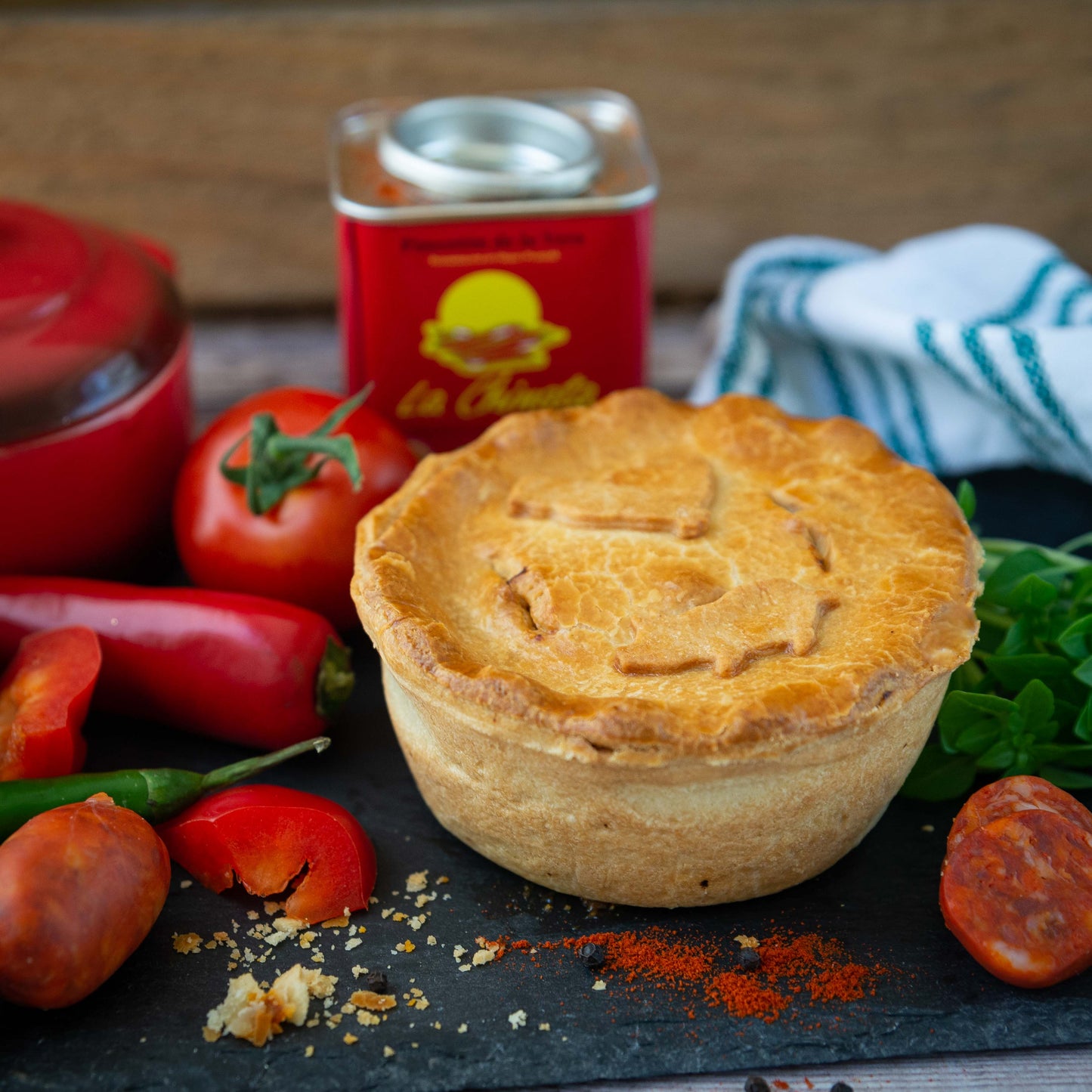 The Mud Pies Chicken and Spanish Chorizo Pie rests golden on a slate board with tomato, chorizo, chilli, basil and paprika nearby.