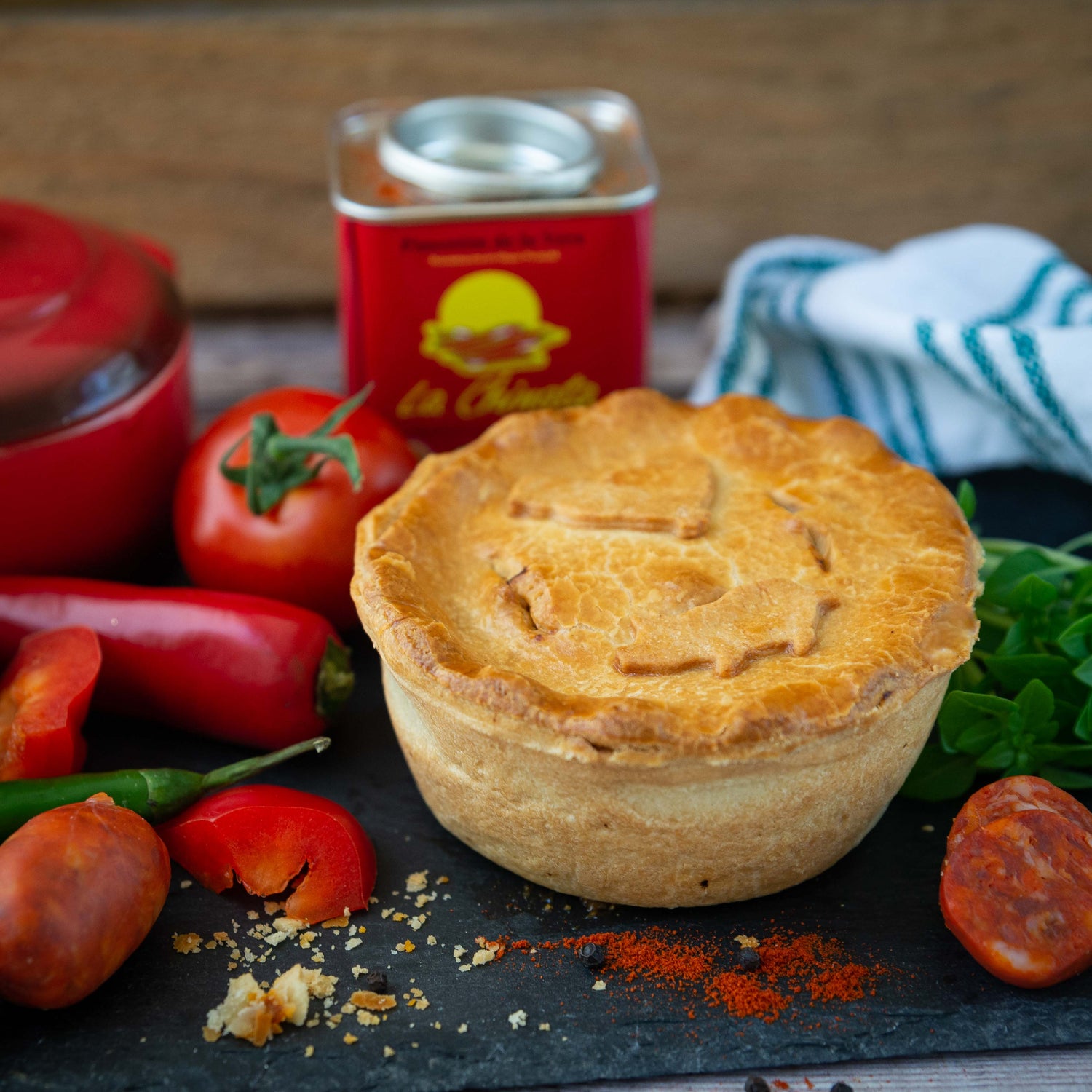 The Mud Pies Chicken and Spanish Chorizo Pie rests golden on a slate board with tomato, chorizo, chilli, basil and paprika nearby.