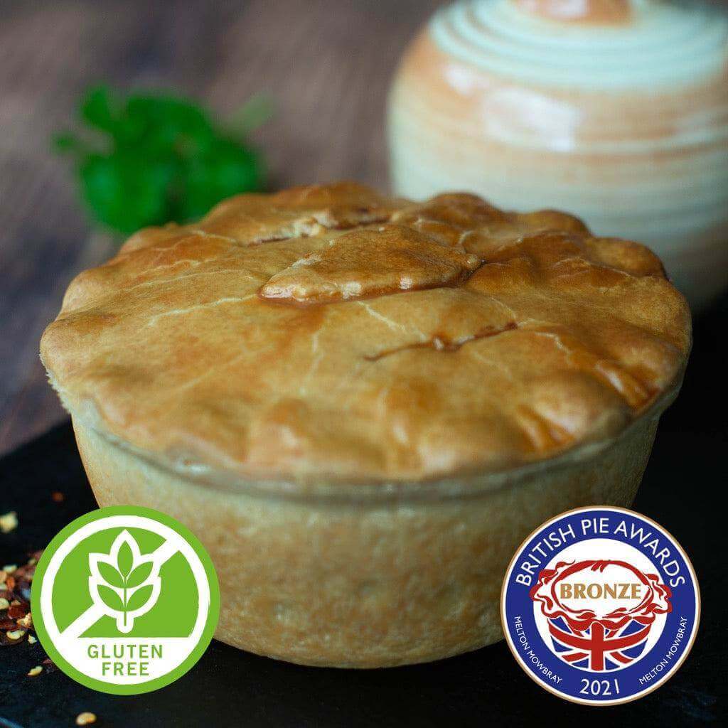 Mud Pies Gluten-Free Chip Shop Chicken Curry Pie, golden-brown, rests on a dark surface with award and gluten-free badges in front.