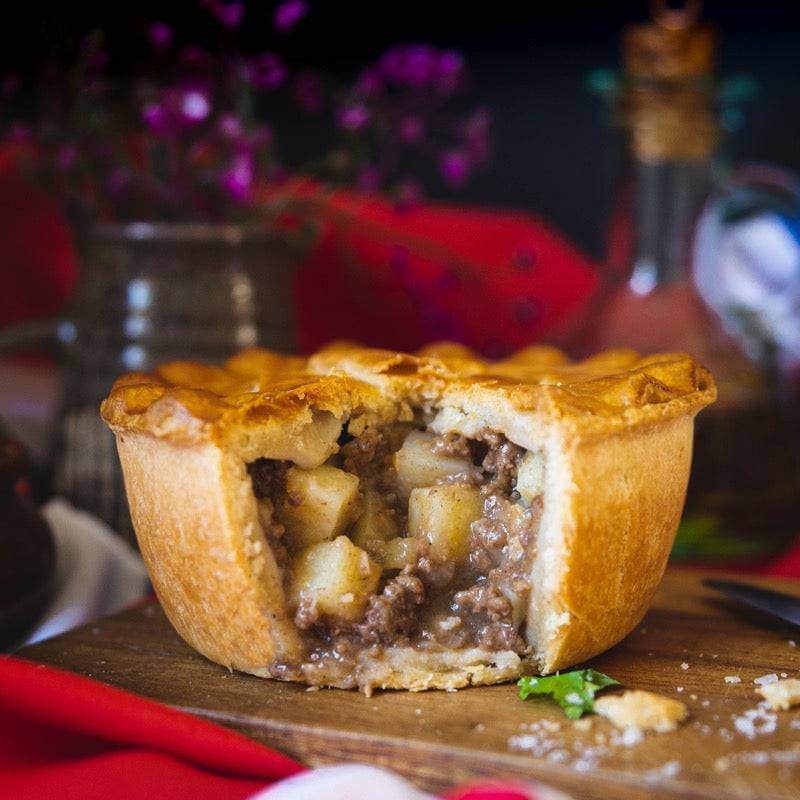 The Mud Pies Hearty Beef and Potato Pie (Meat and Potato Pie) boasts a crisp, golden pastry with tender potatoes and steak in rich gravy, served on wood.