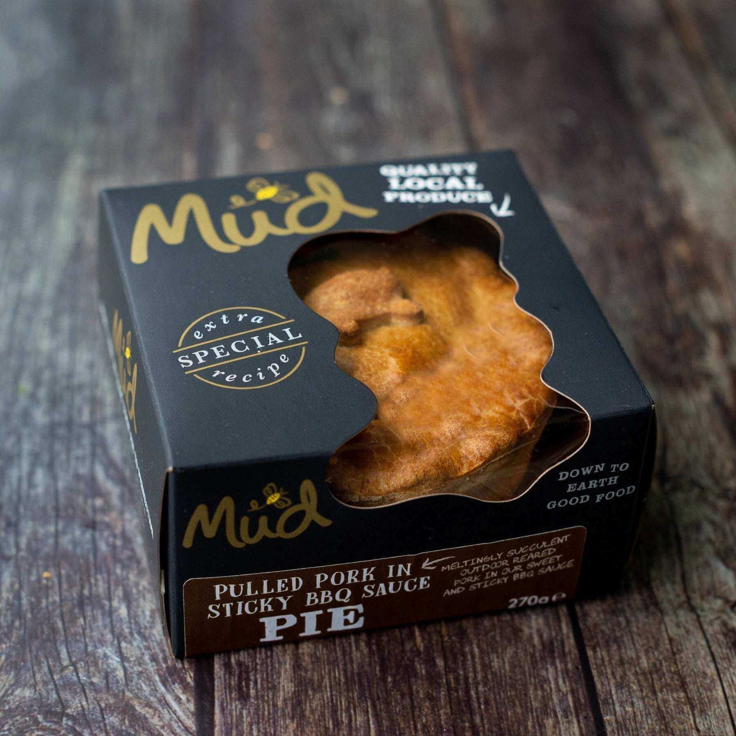 Mud Pies Pulled Pork in Sticky BBQ Sauce pie in a black box with gold and white branding, showing its golden crust on rustic wood.
