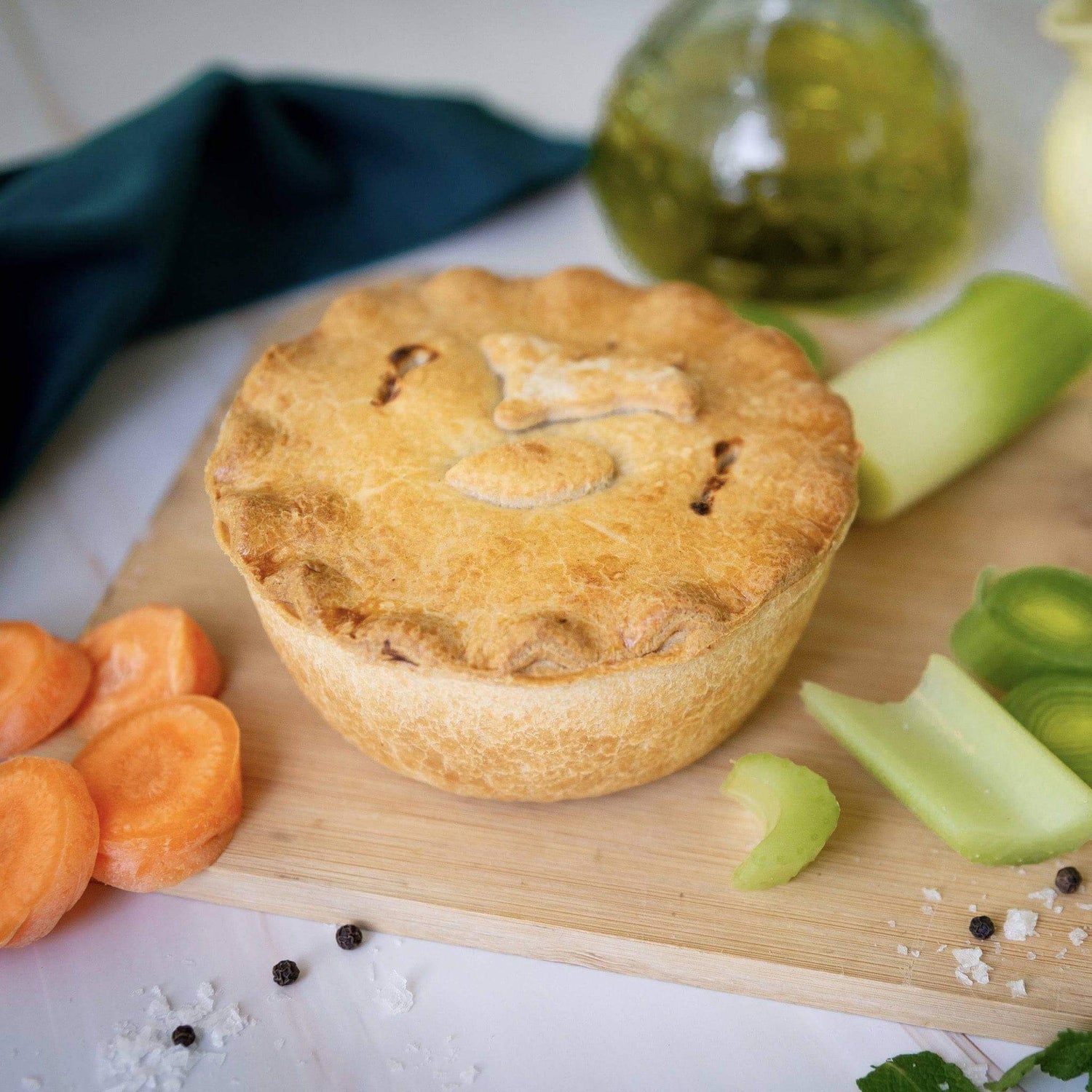 Mud Pies’ Spring Lamb and Mint Pie, topped with a lamb pastry cut out, rests on a wooden board with carrots, leeks, celery, salt and peppercorns.