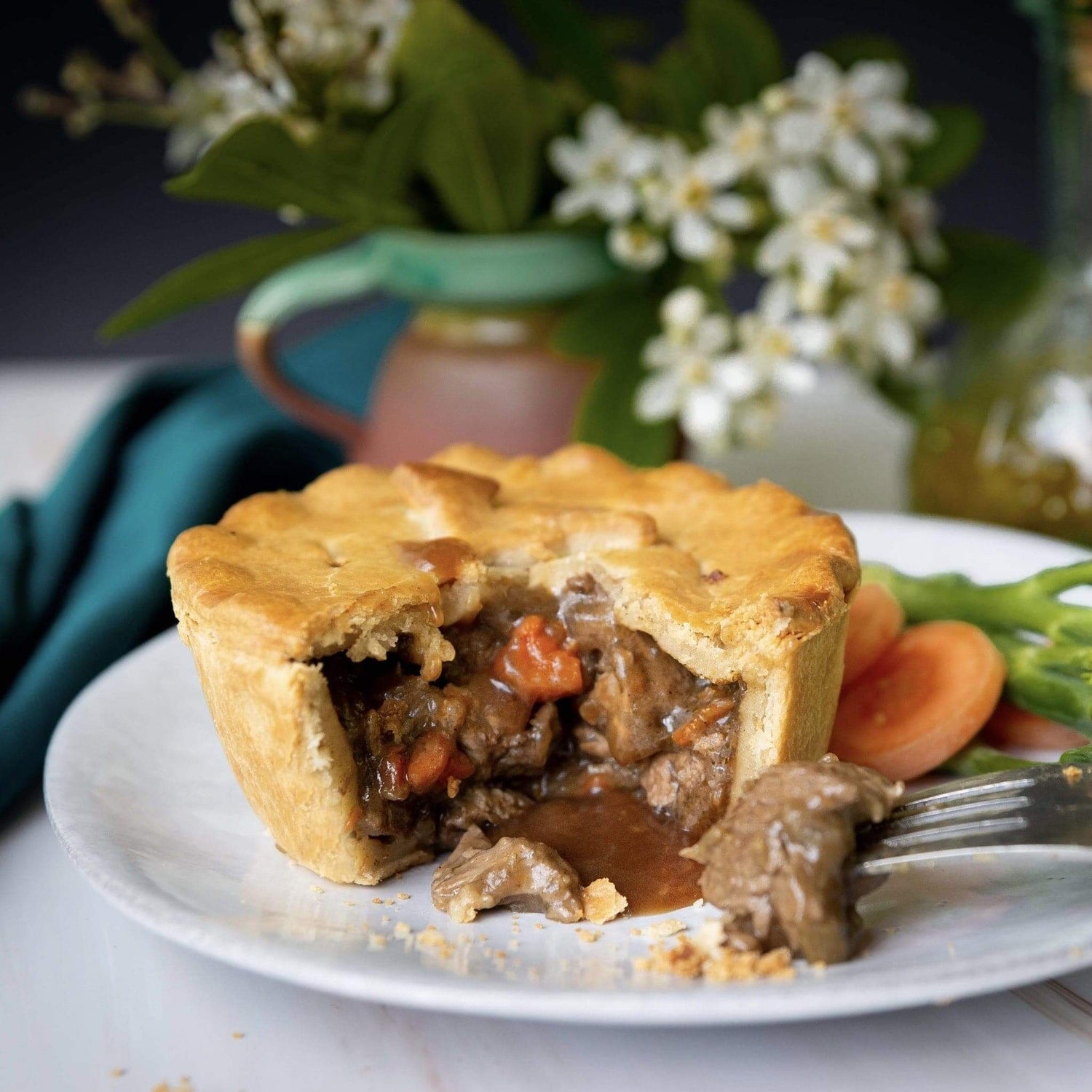 Mud Pies’ Spring Lamb and Mint Pie—golden pastry with Sussex lamb, carrots, mint gravy—on a white plate with beans, tomatoes, fork.