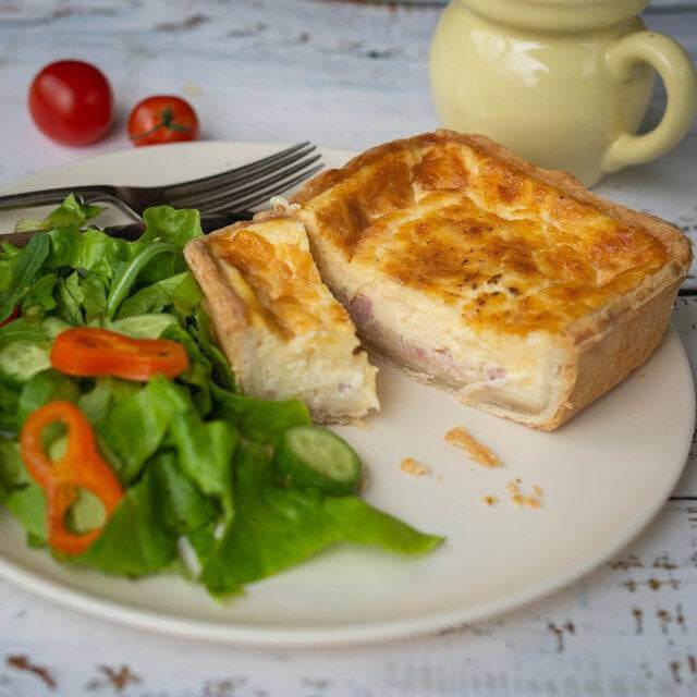 Mud Pies Quiche Lorraine, filled with rich cheddar and British bacon, sits with a crisp cucumber and red pepper salad on a rustic table.