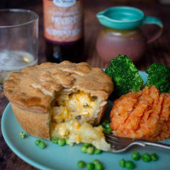 The Mud Pies Gluten-Free Scrumpy Cheese and Onion Pie rests on a plate, its golden crust open to creamy filling, with mash, peas and broccoli.