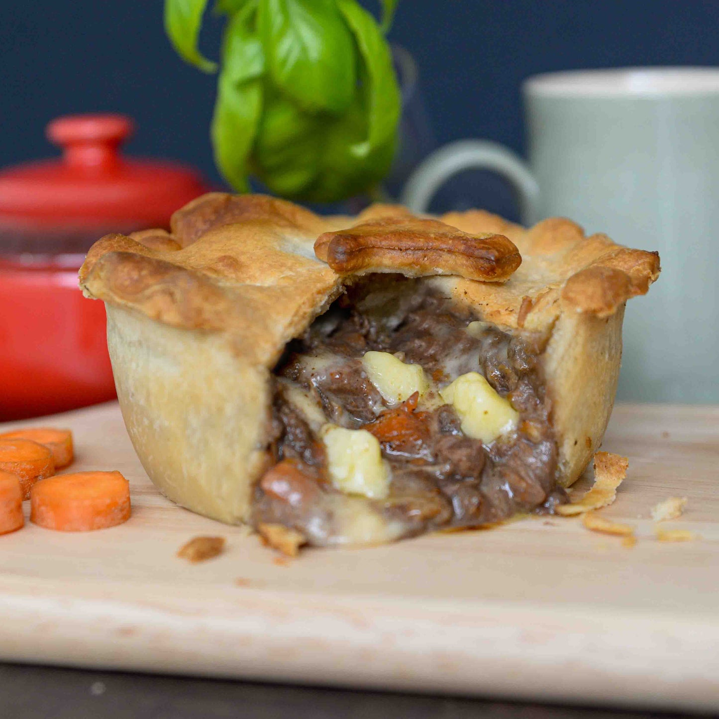 Mud Pies Steak and Cheddar Cheese Pie with a golden, flaky crust sits sliced on a wooden board, showing steak, cheese and carrots.