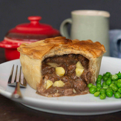 Mud Pies Steak and Cheddar Cheese Pie with a thick, golden crust is sliced open on a white plate, served with green peas.