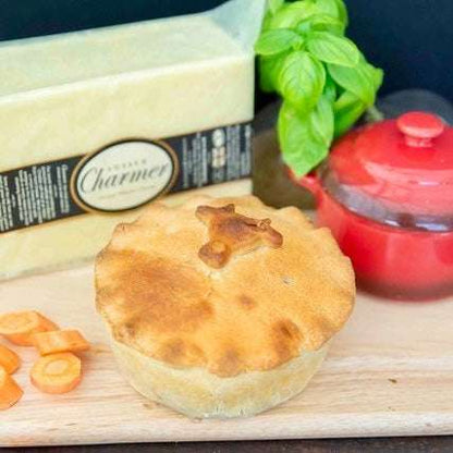 Mud Pies' Steak and Cheddar Cheese Pie, finished with a pastry animal, rests on a wooden board among carrots, cheese, and basil.