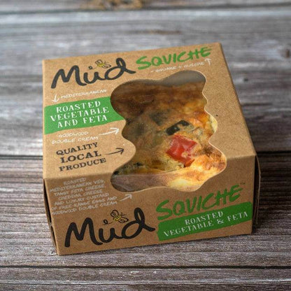 Mud Pies: Roasted Vegetable and Feta Quiche in a cardboard box with handwritten-style script and window, on a wooden surface.