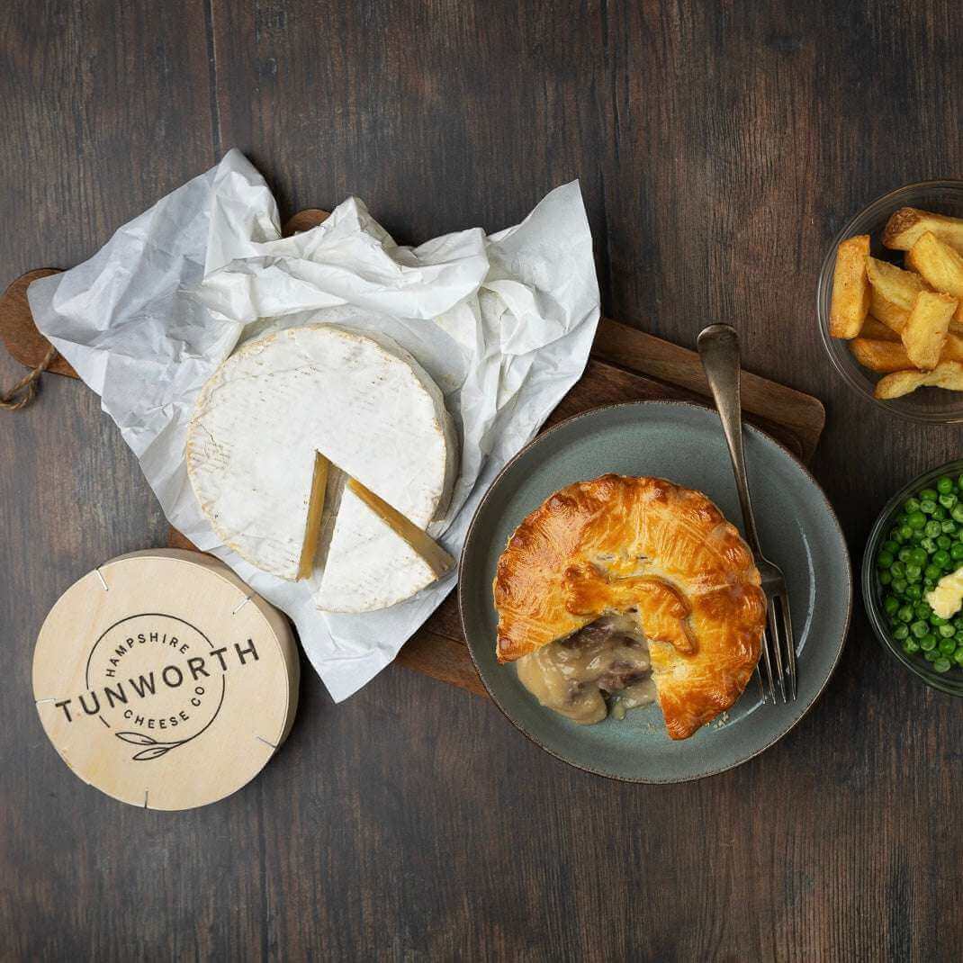 Mud Pies' Steak and Tunworth Cheese Pie is served with golden chips in a yellow bowl, peas in grey, and a soft cheese wheel nearby.